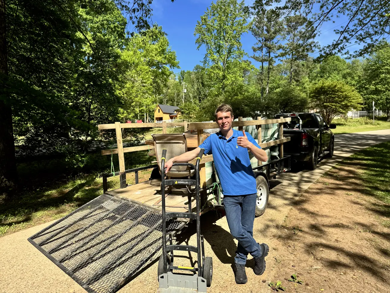 Brayden of Eagle Junk Removal giving a thumbs up beside his trailer, loaded with patio furniture and a hand truck