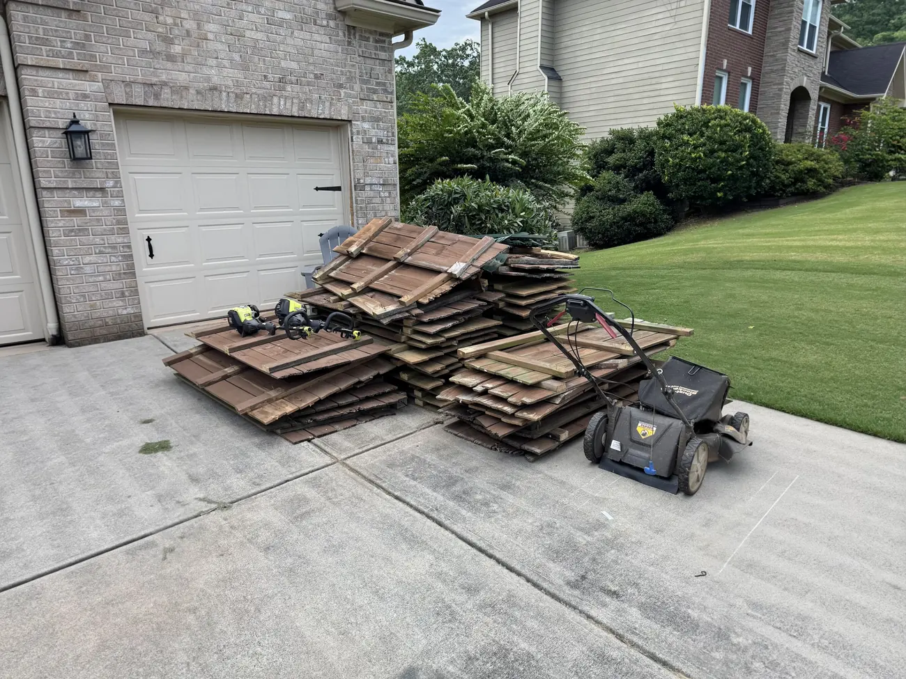 Old fence panels, a lawn mower and two string trimmers piled in a driveway before removal