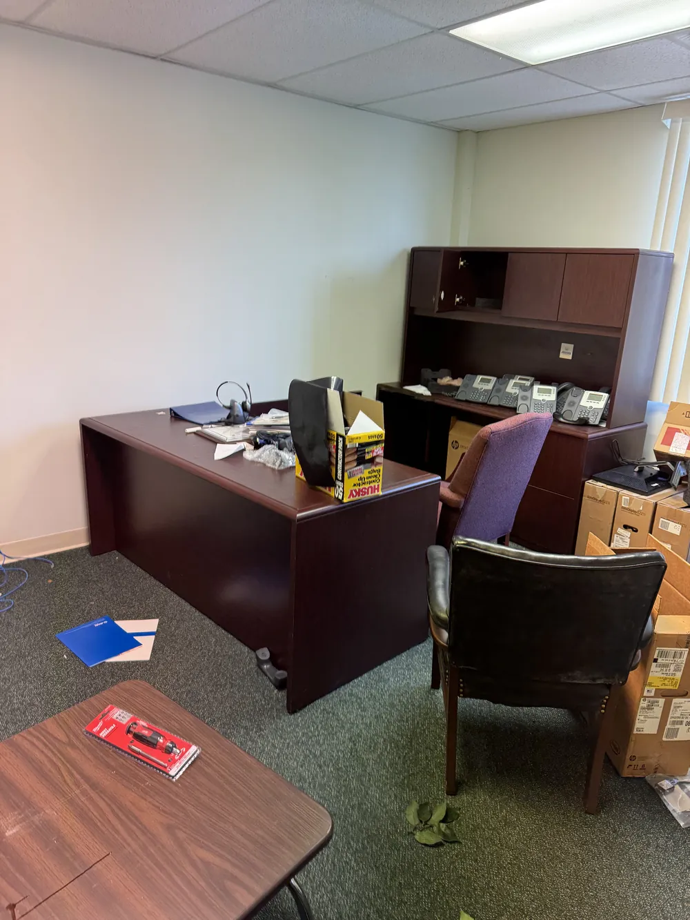 An office with a wooden desk, hutch, chairs, desk phones and boxes before furniture removal